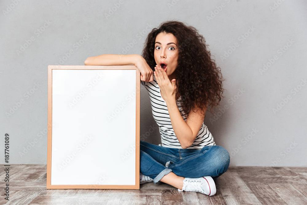 Wall mural funny portrait of adult girl in jeans sitting in lotus pose on the floor expressing embarrassment an