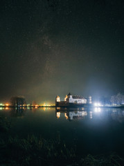 Scenic view of Mir Castle Complex at night with starry sky and glow reflexion on lake. Landmark in Belarus