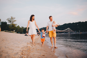 concept family beach vacation. Family of four people mom, dad and brothers children boys walking, want barefoot on the river bank by the hand at sunset in the summer