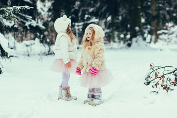 two little girls in fur coats play in the winter forest