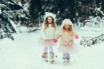 Two kid girls wearing stylish clothes in snow outdoors. Having fun. Winter season. Childhood.