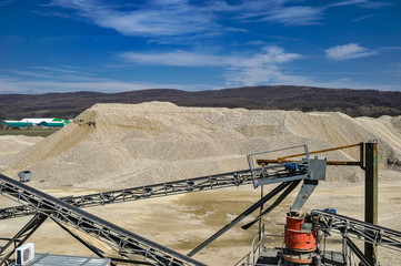 Gravel pit with heavy machineries with blue sky and white clouds on a sunny day.