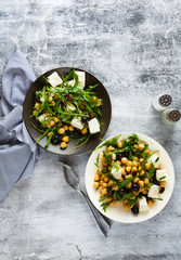 two plates of vegetable salad with chickpeas, arugula, feta cheese or tofu and black olives on a natural stone background. healthy eating