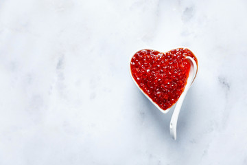 Red Caviar in a bowl in the form of a heart on a white marble table. Valentine's Day Appetizer
