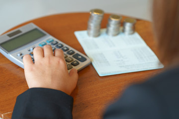 Hands of businesswoman pushing on calculator with account book and coins.