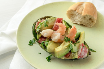 half avocado filled with tomato, shrimp and parsley garnish with a bun on a light green plate, appetizer snack, white tablecloth background with copy space, high angle view from above