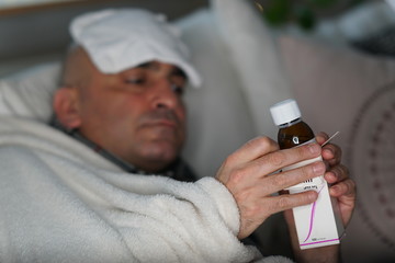 Sick man opening a cough syrup bottle. Selective focus
