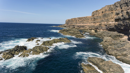 Fototapeta na wymiar Rough sea with waves over rocks by granite cliffs, Atlantic Ocean coast, Fuerteventura, Canary Islands, Spain .