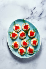 appetizer of red caviar and cheese with dill in a blue plate on white marble