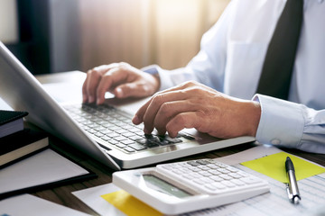 Obraz premium Business man working at office with laptop and documents on his desk. Analyze plans, papers, hands keyboard