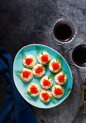 appetizer of red caviar and cheese with dill in a blue plate on a stone background and two glasses of red wine