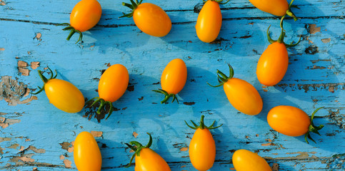 Yellow small tomatoes on blue wooden surface. Flat lay,top view.