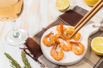 Fried shrimps with chopsticks on a white wooden board
