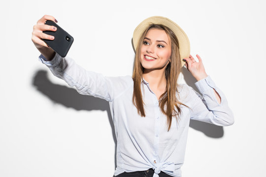 Portrait of a young attractive woman with hat making selfie photo on smartphone isolated on white background
