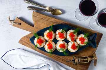 festive serving of red caviar sandwiches on a plate in the form of fish on a white stone background on a wooden board and two glasses with red wine