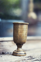 An ancient brass wineglass with an ornament from India stands on a wooden half-shell.