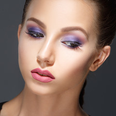 Fashion beauty portrait of a beautiful girl with a lilac make-up isolated on a gray background.