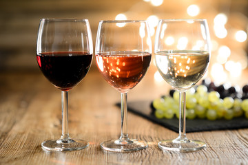 three glass of white red and rose wine with dim light in wooden restaurant table with a grape background