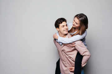 Playful couple riding piggy back together laughing as they young woman rides on her husbands piggy back, on grey background
