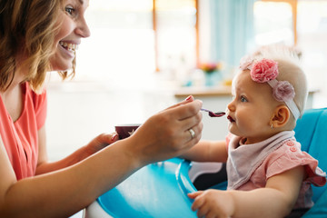 Mother feeding baby with spoon indoors