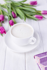 White cup with coffee cappuccino, book and purple tulips on a white background. Free space