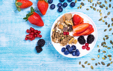 Breakfast  fruit bowl with yogurt ,strawberries , blueberries , blackberries , cranberry and assorted cereals flat lay top view - Healthy nutrition concept on vintage blue wood background with seeds