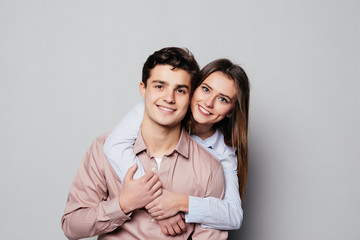 Fototapeta premium Portrait of a cheerful young couple hugging while standing and looking at camera over gray