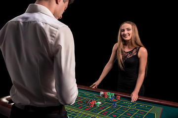 A close-up on the back of the croupier in a white shirt, image of green casino table with roulette and chips, a rich woman betting of gambling in the background