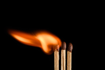 Three matches and one of them is in the process of ignition on a black background closeup