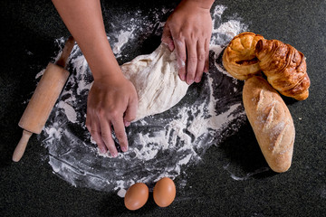 Raw dough for bread with ingredients on black background, male hands kneading dough sprinkled with...
