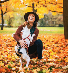 Happy young woman playing with dog outdoors in autumn