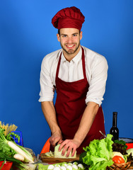Chef with smiling face chops cabbage with knife on blue