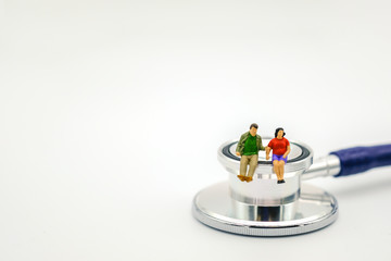 Health Care Concept. Fat man and fat woman miniature figures sitting on Stethoscope on white background with copy space for text