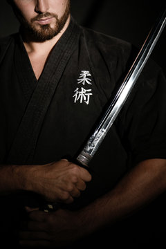 man practicing ju-jitsu in a black kimono carrying a japanese sword, called la&iuml;to