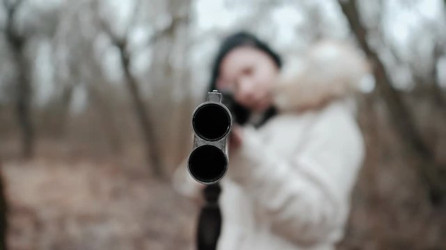 Hunter woman wearing warm coat targets the enemy on the battlefield with rifle. Unrecognizable girl training with a shotgun weapon in autumn forest. Slow motion. Focus on barrel