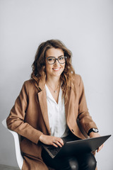Smiling beautiful business woman in a glasses with a laptop in the office near a white wall