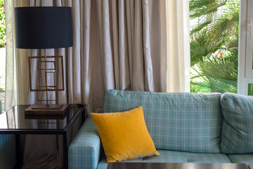 Modern home living room interior decor design. Sky blue checked herringbone patterned couch sofa. Yellow velvet cushion pillow. Black table lamp.