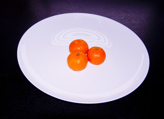 three tangerines on a white plate
