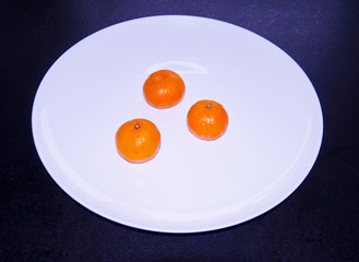 three tangerines on a white plate