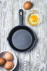 Empty cast iron skillet and raw eggs in a bowl on white background. Top view, space for text.