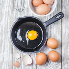 Raw egg in cast iron skillet on white wooden background. Top view, space for text.