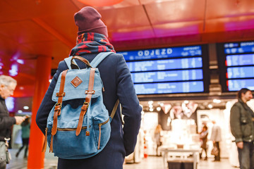 Obraz premium Woman waiting on the station platform with backpack on background of schedule
