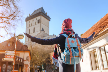 Woman traveler with backpack looking at the medieval gothic castle Karlstejn in Czech Republic.