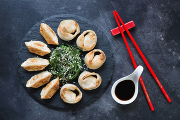 Pan fried asian dumplings served on a stone slate with chuka salad and dipping sauce. Flat-lay on a dark scratched metal background, horizontal shot