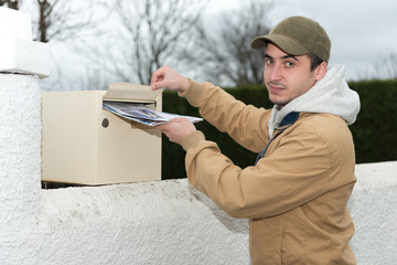 man putting newspaper from the mailbox