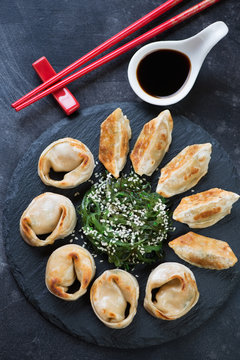 Above view of fried asian dumplings with seaweed salad and soy sauce on a stone slate tray, vertical shot, close-up
