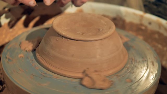 A potter carves the foot of a new bowl. 