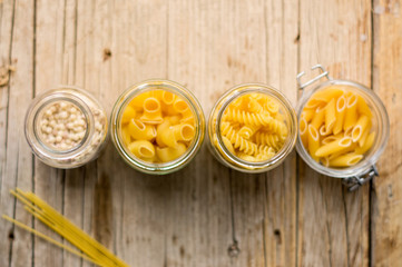 Top view of assortment of italian dry pasta in glass containers on a wooden table