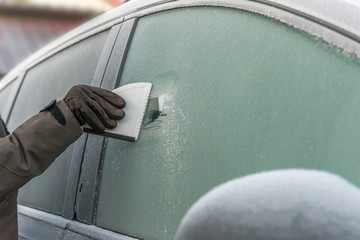 Scraping ice from frozen car windshield or side window. Closeup of scraping with a ice scraper....