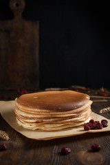a pile of pancakes, berries, biscuits and a cutting board on parchment on a dark wooden table